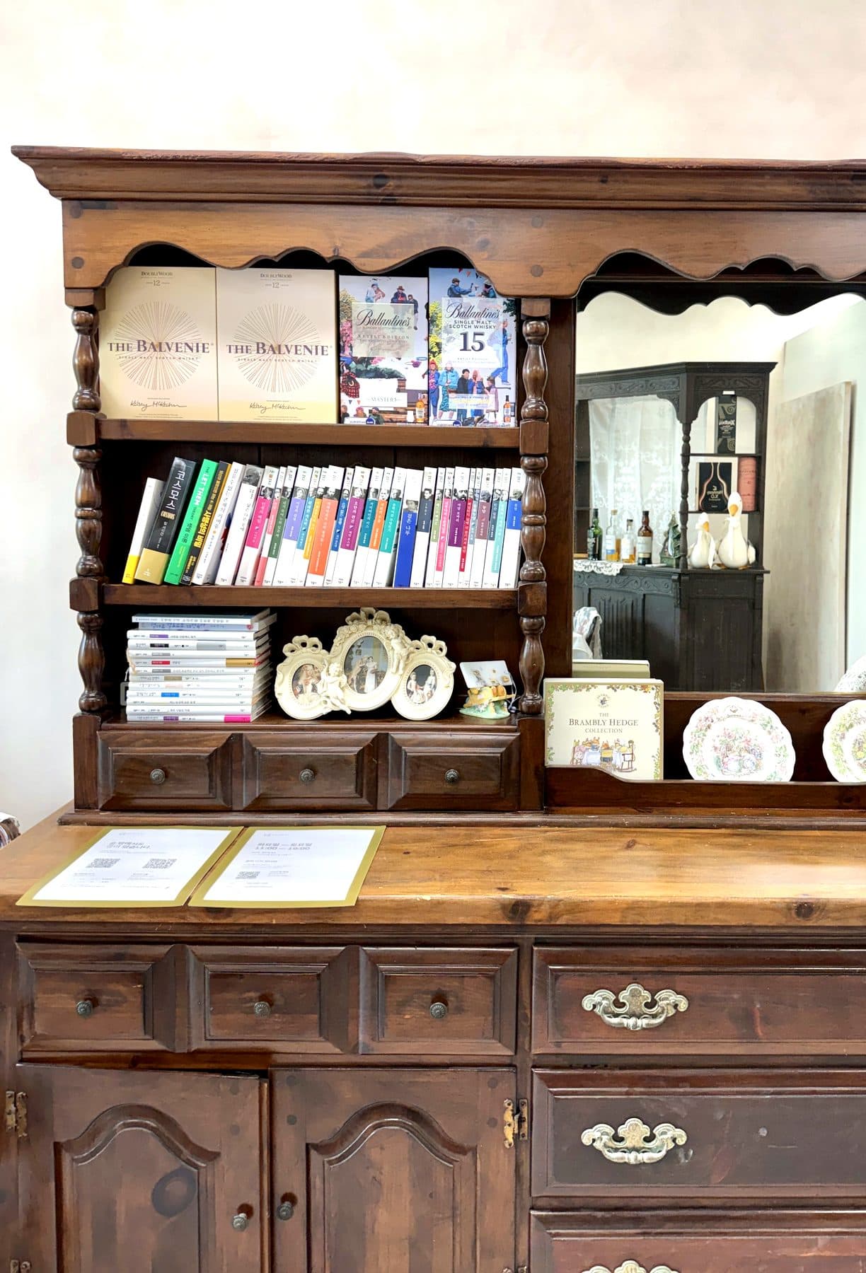 Des livres sur une étagère en bois aux arches répétées, un cadre en porcelaine à côté, et le cabinet reflété dans le miroir voisin